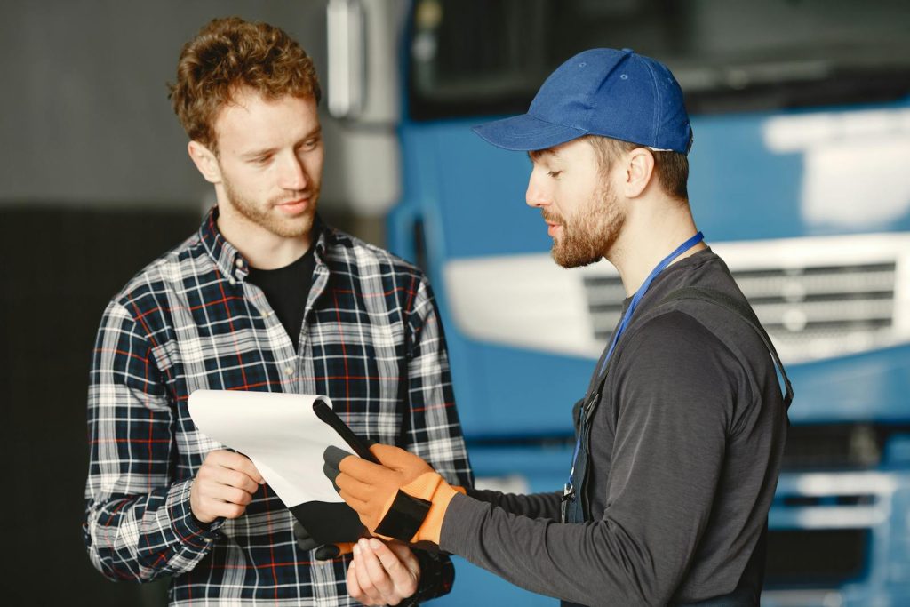 Mechanic in uniform talks with a customer about vehicle maintenance inside a garage.